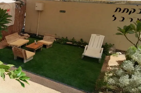 פינת צ׳יל משותפת — מדשאה, ספסלי עץ מרופדים ומיטת שיזוף
